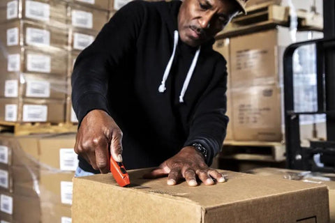 Person using Auto Retracting Safety Utility Knife with Quick Change Blades, Thumb Bridge Grip on cardboard box