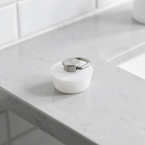 White Silicone Sink Stopper with Stainless Steel Ring for Bathtubs positioned on a gray countertop.
