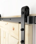 Close-up of 6 ft sliding barn door hardware kit with black track, 1/4 inch carbon steel rails, and J shape wheel system installed on a wooden door.