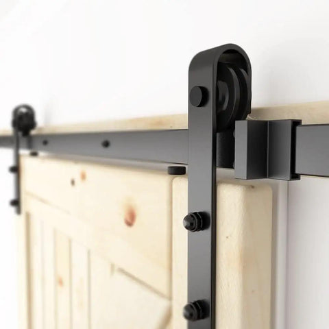 Close-up of 6 ft sliding barn door hardware kit with black track, 1/4 inch carbon steel rails, and J shape wheel system installed on a wooden door.