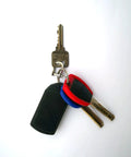Three keys on a keyring including a flat black key fob and two colored keys against a white background.
