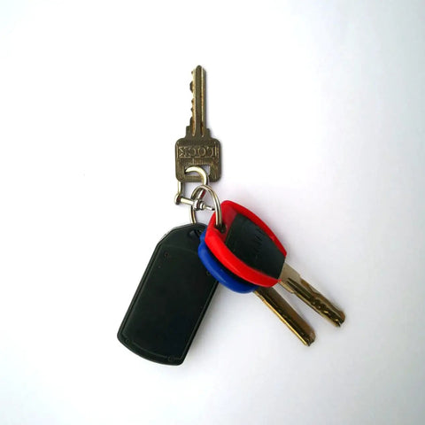 Three keys on a keyring including a flat black key fob and two colored keys against a white background.