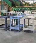 Three utility carts in a warehouse setting, showcasing the Two Shelf Foam Utility Cart With Lipped Shelves And Ergonomic Handle Black 500 Lb Capacity Durable Rolling Cart For Warehouse Garage Cleaning And Manufacturing Environments Heavy Duty Construction For Long Lasting Service In Demanding Workspaces.