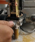 Close-up of a four-port air compressor pressure switch control valve with a red on/off knob being installed on a compressor unit.