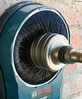 Front view of Bosch circular brush wheel attached to blue drill against a brick wall.