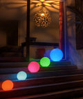 Five Ultra Fun Waterproof 10 Inch RGB LED Ball Light Orbs on steps with colored glow at night, perfect for outdoor decor.