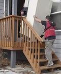 Side view: two workers use a padded Shoulder Dolly 3500 two-person lifting system to move a large appliance up outdoor stairs