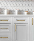 Set Of Ten 4 Inch Center Hole Brushed Brass Cabinet Pulls installed on white kitchen cabinets with hexagon tile backsplash.