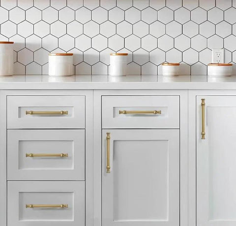 Set Of Ten 4 Inch Center Hole Brushed Brass Cabinet Pulls installed on white kitchen cabinets with hexagon tile backsplash.