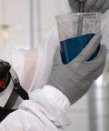Person in Fresh White Nylon Spray Paint Coveralls With Kickback Ready Lint Free Construction mixing blue paint in a cup.