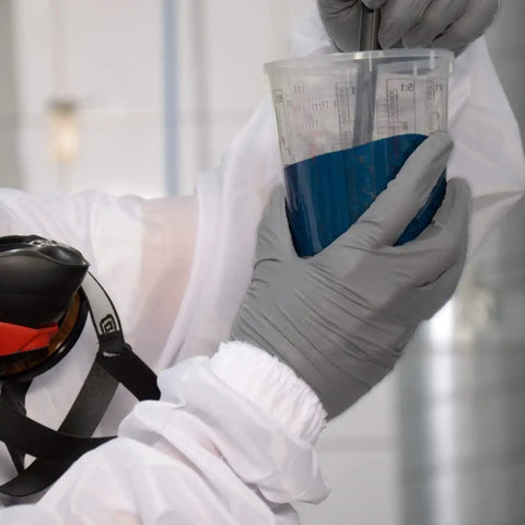 Person in Fresh White Nylon Spray Paint Coveralls With Kickback Ready Lint Free Construction mixing blue paint in a cup.
