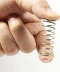 Close-up of stainless steel compression spring held between fingers; small DIY repair spring.