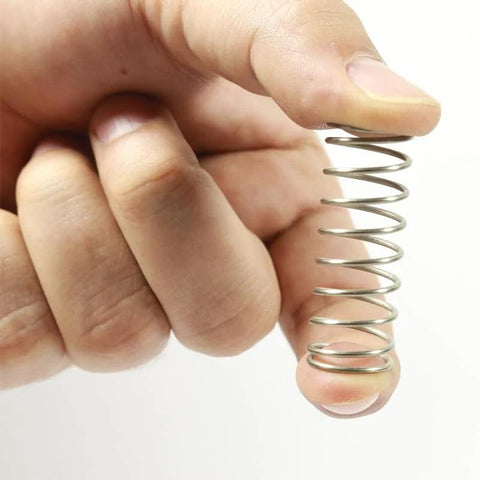Close-up of stainless steel compression spring held between fingers; small DIY repair spring.