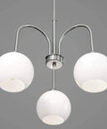 Carisa Three Light Chandelier in brushed nickel with glossy white glass globes hanging from ceiling.