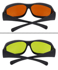 Professional Grade Kickass Laser Safety Glasses With Hella Od5 Plus Eye Defense Across One Hundred Ninety To Eleven Hundred Nanometer Wavelength Range For Spa Studios And Beauty Clinics In Classic Orange Lens both orange and green lenses shown, black frame, crossed behind.