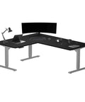 Rock Solid L Shaped Electric Standing Desk Height Adjustable Corner Workstation Table Designed For Heavy Multi Monitor Setups With Whisper Quiet Adjustment System Premium Ebony Oak Surface And Durable Gray Frame For Ultimate Office Vibes with laptop and monitor setup.
