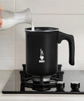 Tutto Crema Milk Frother Black Barista Grade, 1L Capacity on stovetop with milk being poured, not compatible with induction.