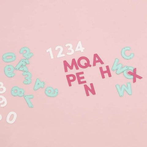 Die cuts of numbers and letters on pink surface, part of Number Shaped Die Cut Set, 0 Through 9, For Card Making And Scrapbooking