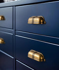 Six Pack 3 Inch Antique Brass Cup Pulls With Textured Strap Design installed on navy cabinet drawers