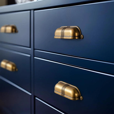 Six Pack 3 Inch Antique Brass Cup Pulls With Textured Strap Design installed on navy cabinet drawers