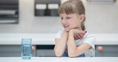 Child observing a glass of clear water on a kitchen counter, illustrating water purity.