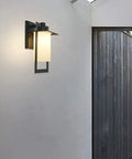 Top Tier Modern Outdoor Wall Sconce Featuring Waterproof Black Matte Aluminum Bracket And Cylindrical Glass Shade on wall.