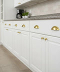 Brushed Gold Cup Drawer Pulls 3 Inch 76mm Set of 10 installed on white kitchen cabinets, showcasing elegant design and durable metal finish.