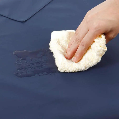 Hand wiping water from Waterproof Rubber Vinyl Apron With Two Big Pockets For Dishwashing And Grooming Lightweight PU Workhorse Apron