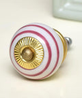 No Fuss White Ceramic Drawer Knobs 100 Piece Set Featuring Striped Motif For Kitchen Cabinets And Dresser Pulls close-up of round white knob with pink stripes and golden base.