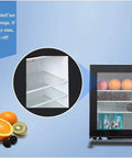 Compact Upright Mini Freezer Featuring A Sleek Black Glass Door With Energy Efficient Cooling That Runs Dead Quiet At Twenty Eight Decibels Ideal For Dorms Offices Or Small Bedrooms With Plug And Play Design showcasing the glass shelves and fruits inside.