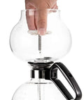 Close-up of hand assembling 8 Cup Stovetop Siphon Coffee Maker For Rich Vacuum Brew, 24 Oz Heat Resistant Borosilicate Glass Durable Glass Construction.