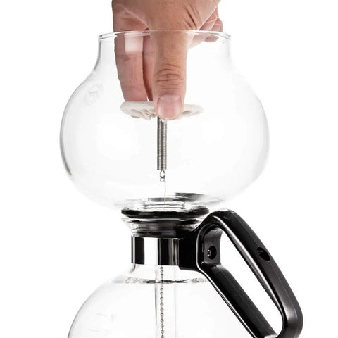 Close-up of hand assembling 8 Cup Stovetop Siphon Coffee Maker For Rich Vacuum Brew, 24 Oz Heat Resistant Borosilicate Glass Durable Glass Construction.