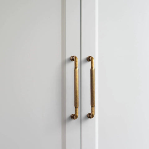 Antique Brass Cabinet Pull Handles Six Pack 5 Inch Vintage Vertical Grooved Textured Grip on white cupboard doors.