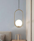 BEQAOR Modern Globe Pendant Light, 1-Light Oval Hoop Hanging Ceiling Fixture with Frosted White Glass Shade and Gold Finish Frame for Bedroom Bedside, hung over a bedside table.