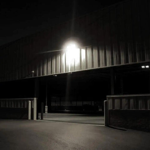 Dusk to Dawn LED Security Light 18W illuminating a dark garage exterior, showcasing the brightness of the adjustable two-head wall mount.