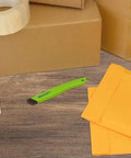 Front view of green Westcott ceramic box cutter with safety blade on a desk near yellow envelopes.