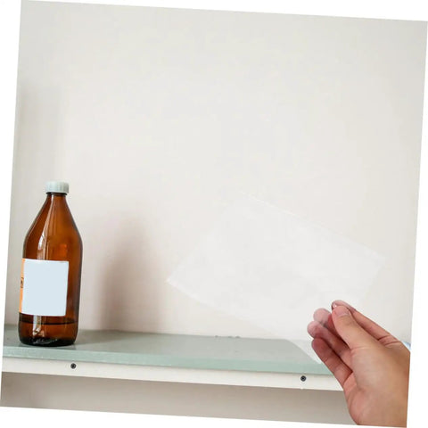 Hand holding a cellophane film sheet next to a brown bottle, part of the Hands-On Osmosis Demonstration Kit With 12 Cellophane Lab Sheets And Glassine Paper For Classroom Experiments, Semipermeable Membrane Films For Clear, Realistic Osmosis Demos In Middle And High School.
