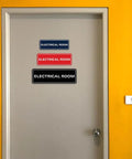 Black Electrical Room Sign Easy To Read For Doors Panels And Walls Keeps Staff And Emergency Pros In The Know About Electrical Rooms Compliant Durable Available In 2x6 And 2.75x7 And 3x9 Inches. Black electrical room sign on gray door, adhesive-backed, shown in 3 sizes.