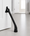 Heavy Duty Kickdown Door Stopper With Extended Reach Design And Rock Solid Zinc Alloy Frame For Tight Grip Non Slip Rubber Foot mounted on a white door.