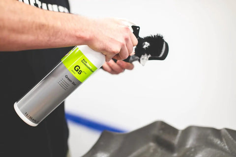 Person using a spray bottle with a brush on a car mat; product similar to All In One Car And Workshop Universal Cleaner Highly Concentrated