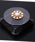 Solar Powered Rotating Jewelry Display Stand With Built In Kickstand showcasing a gold floral brooch on a clear turntable.