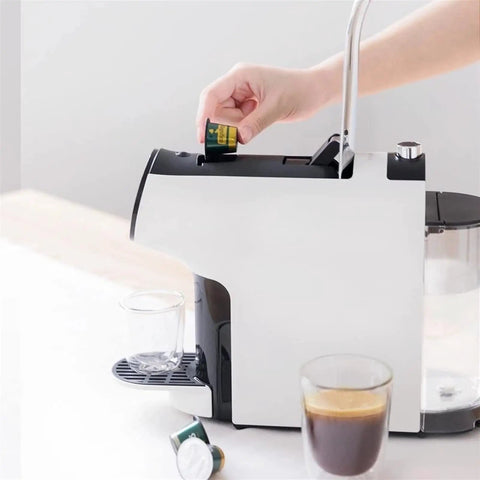 Hand inserting capsule into Compact Smart Automatic Capsule Coffee Machine With Grind And Brew Tech One Touch Espresso Maker For Your Home Office Brews Ground Or Whole Bean Coffee Keeps Coffee Hot For 40 Minutes Multi Flavor Options, with cups filled.