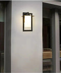 Top Tier Modern Outdoor Wall Sconce Featuring Waterproof Black Matte Aluminum Bracket And Cylindrical Glass Shade mounted on a wall.