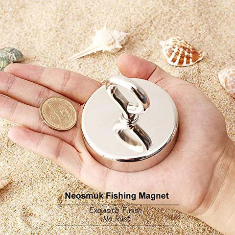 Front view of Neosmuk fishing magnet with lifting ring, chrome finish, held in hand on sandy beach.