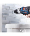 Bosch blue cordless drill side view with attached bit near a tiled wall.