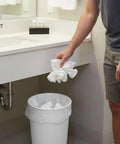 Person throwing used paper towels into a white trash can lined with No Mess Clear Trash Bags Bulk Bundle One Thousand Count Seven To Ten Gallon.