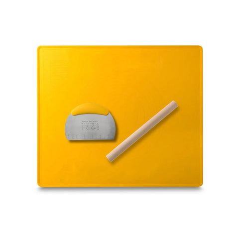 Yellow silicone baking mat with metal scraper and wooden rolling pin.