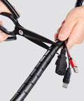 Cutting 10m Black Spiral Cable Sleeve For Pet Proof Cord Management And Desk Wire Protection Kit with scissors, showing wire organization