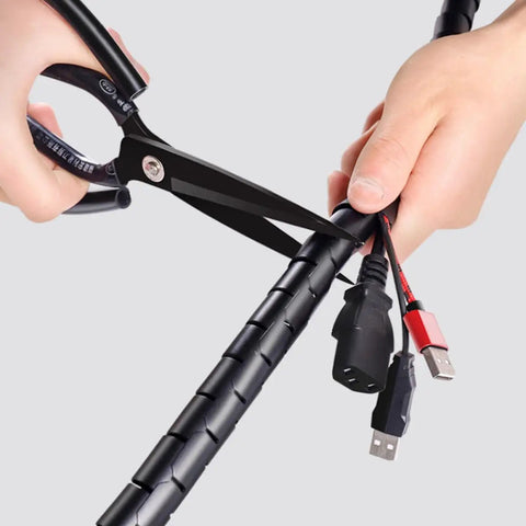 Cutting Pet Proof Spiral Cable Sleeve 22mm Black 10m with scissors, revealing protected computer power cords and connections.