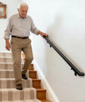 Step Up Your Game With This Four Foot Aluminum Handrail Kit For Indoor And Outdoor Stairs Featuring Hella Tough Matte Black Finish Quick Snap Stainless Brackets And ADA Compliant Grip used by an elderly man on a staircase.